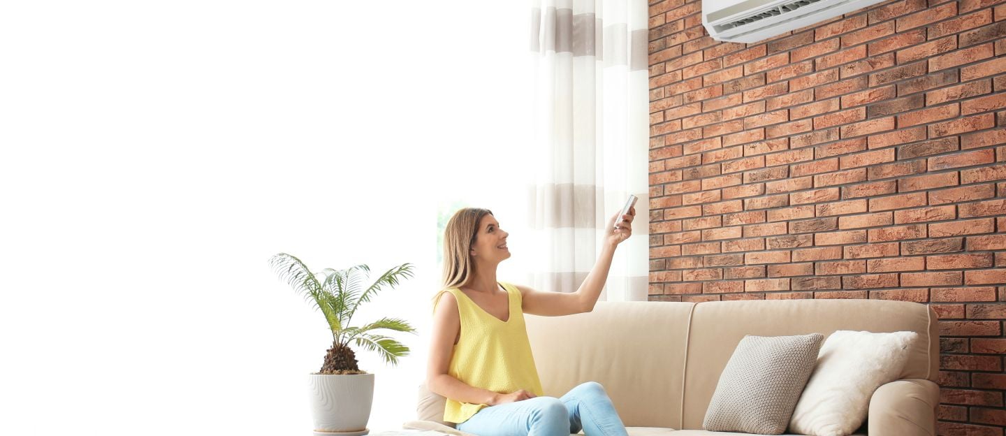 Woman,Operating,Air,Conditioner,While,Sitting,On,Sofa,At,Home