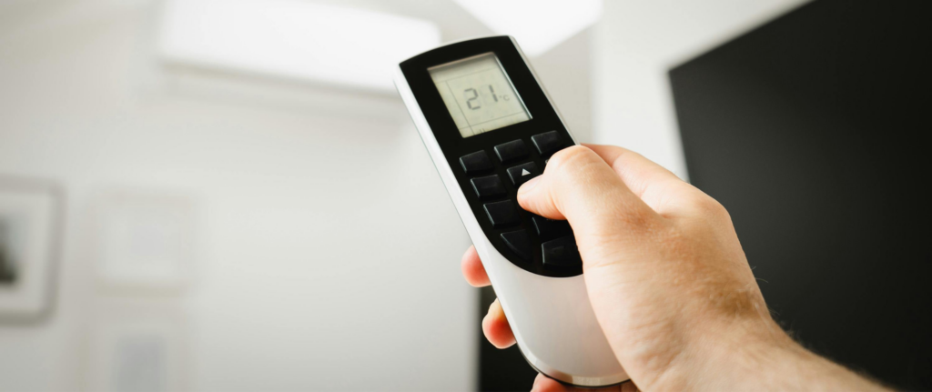 seseorang sedang memegang remote ac dengan indikator suhu 21 derajat