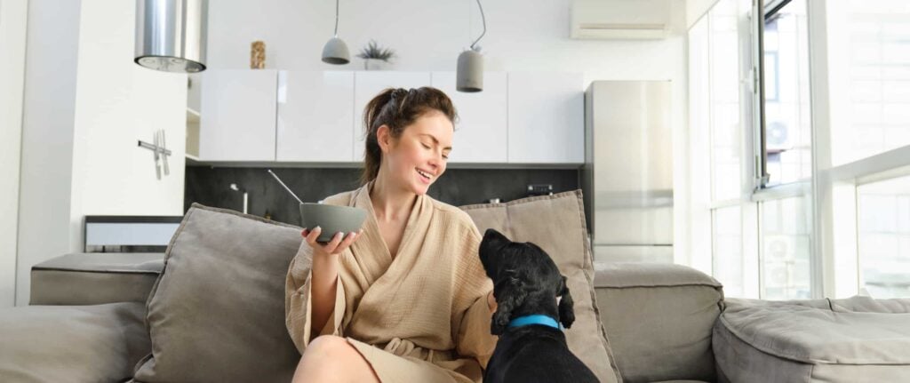 wanita di dalam ruangan memegang mangkuk dan bercengkrama dengan anjing warna hitam