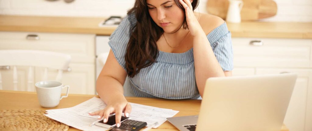 seorang wanita sedang menghitung sesuatu di kalkulator dengan ekspresi bingung