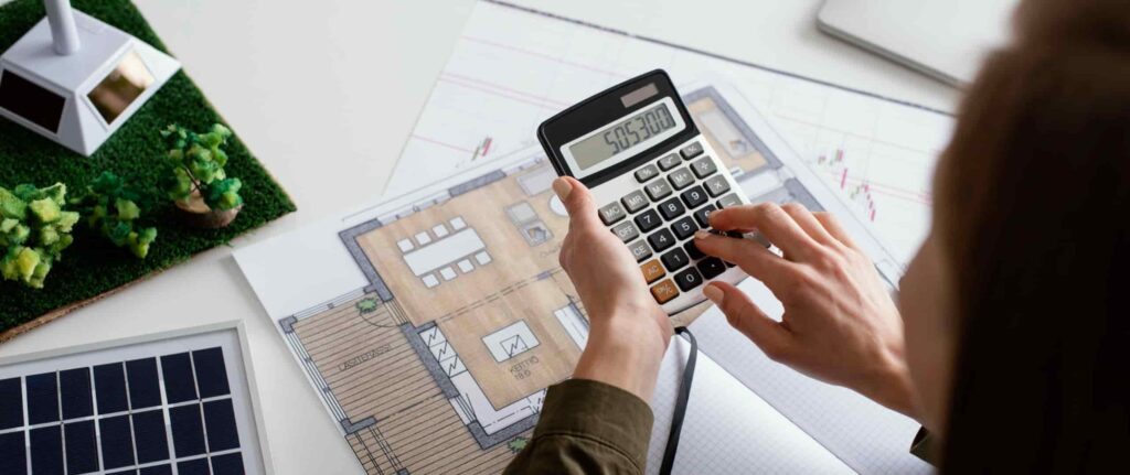 wanita menghitung sesuatu di kalkulator dan ada sketsa bangunan di atas meja
