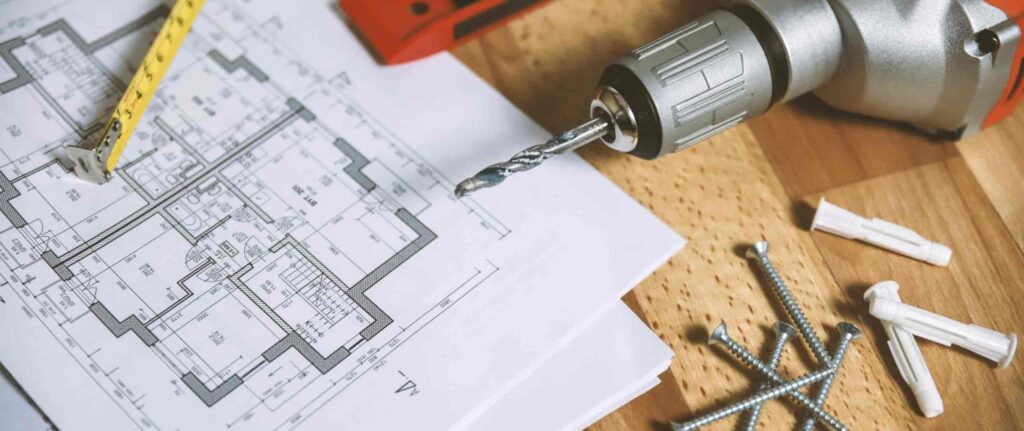 denah rumah, alat bor, meteran, dan lainnya di atas meja