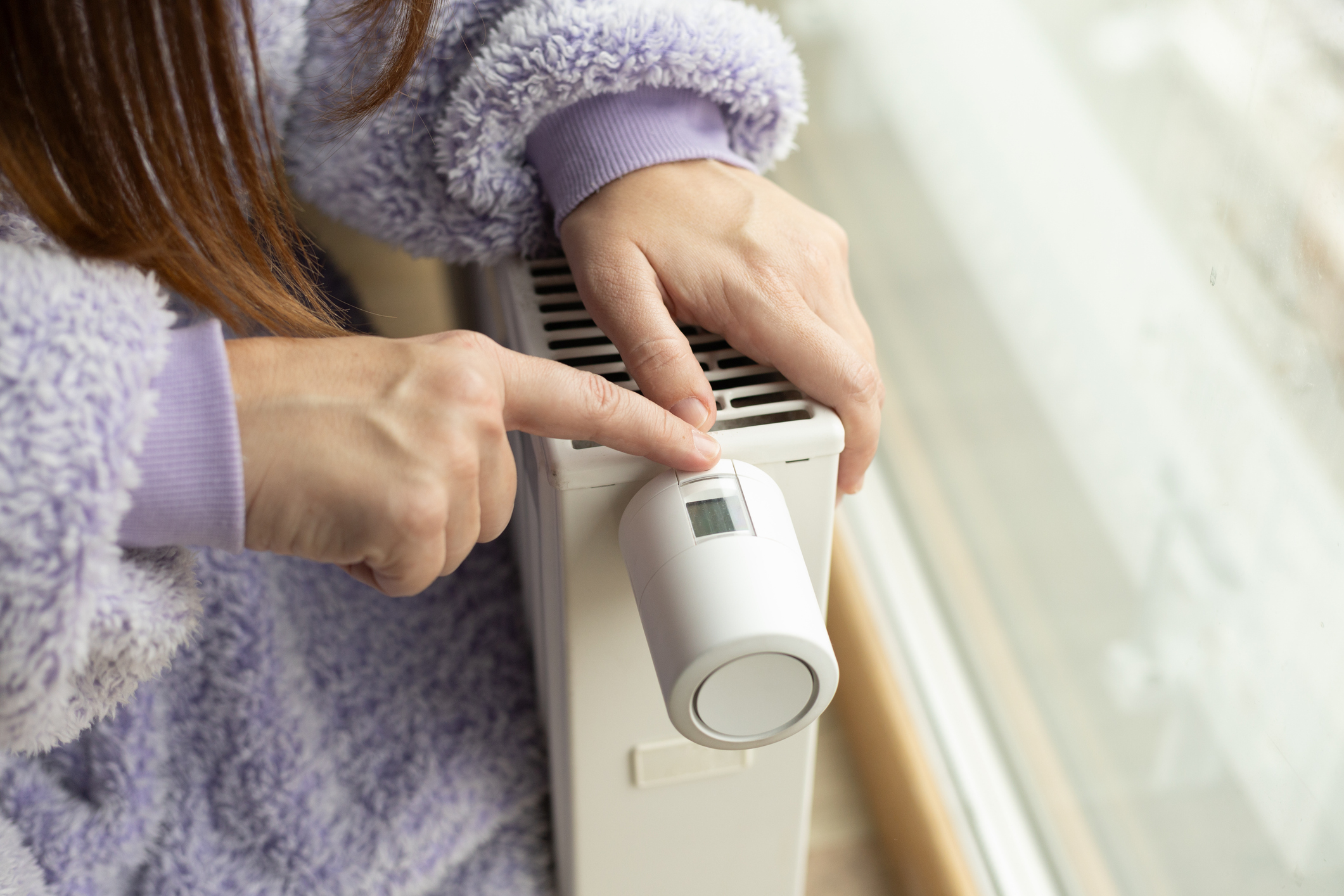 female hand on radiator, one hand pointing to thermostat