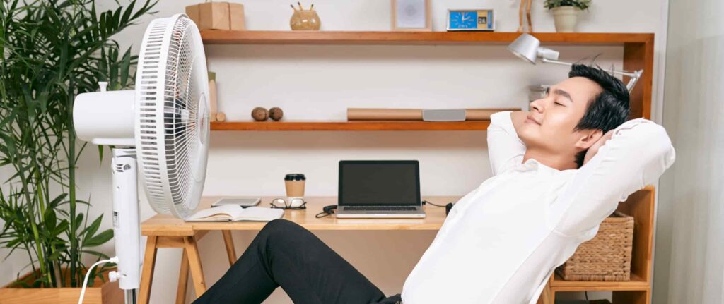 orang yang bersantai di meja kerja sambil menikmati angin dari kipas angin orang yang bersantai di meja kerja sambil menikmati angin dari kipas angin