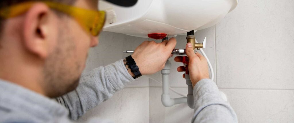 teknisi yang memperbaiki unit pemanas air bagian bawah