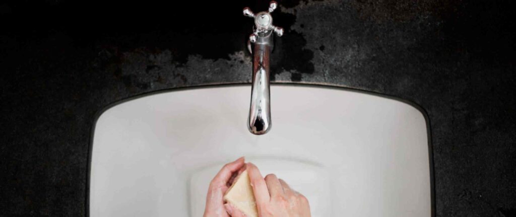seseorang sedang memakai sabun batang di wastafel dengan keran air putar